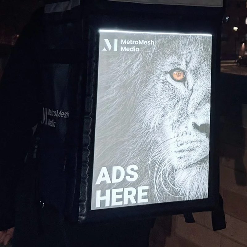 Lit MetroMesh display bag reading Ads Here on a city street at night